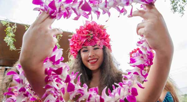 A smiling woman with a pink lei in her hands