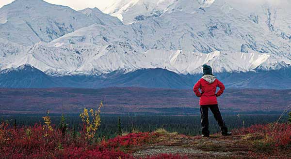 Woman in a red jacket stands in awe of Alaska's mountains
