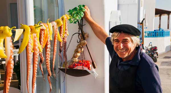 A Mediterranean man smiles while hanging fruit to dry.