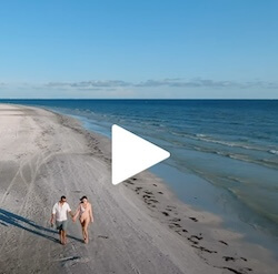 A video still of a couple walking on a beach hand in hand.
