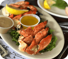 A platter of cooked stone crab claws garnished with lemon and accompanied by two small cups of dipping sauce.