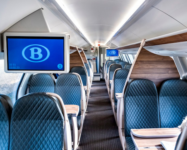 The interior of an SNCB train with padded blue leather seats in paris, tables and wooden panelling