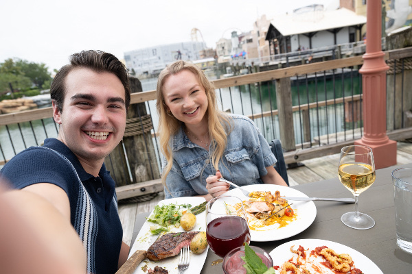 A man and woman enjoying dinner and wine at an outdoor table overlooking the water at Lombards Seafood Grill in Universal Studios Florida.