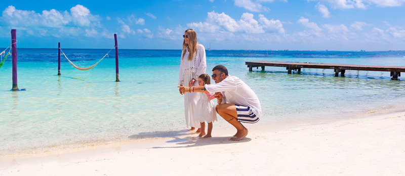 Family walking on a white sand beach with the Caribbean Sea and water hammocks behind them